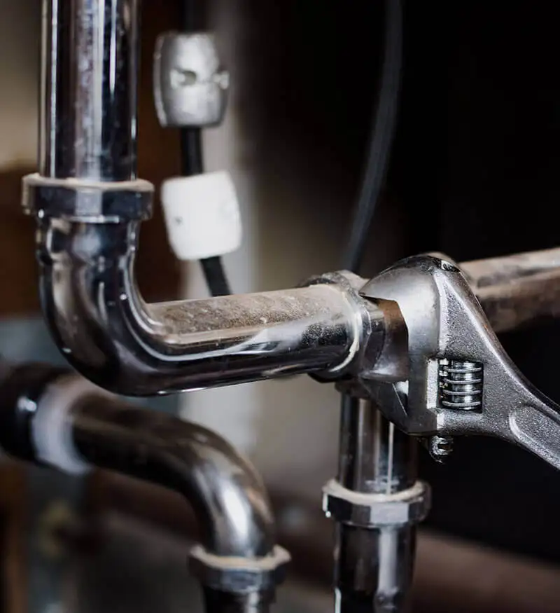 plombier_urgence_24_M Plombier professionnel réparant une fuite d'eau sous un évier dans une maison à Bruxelles